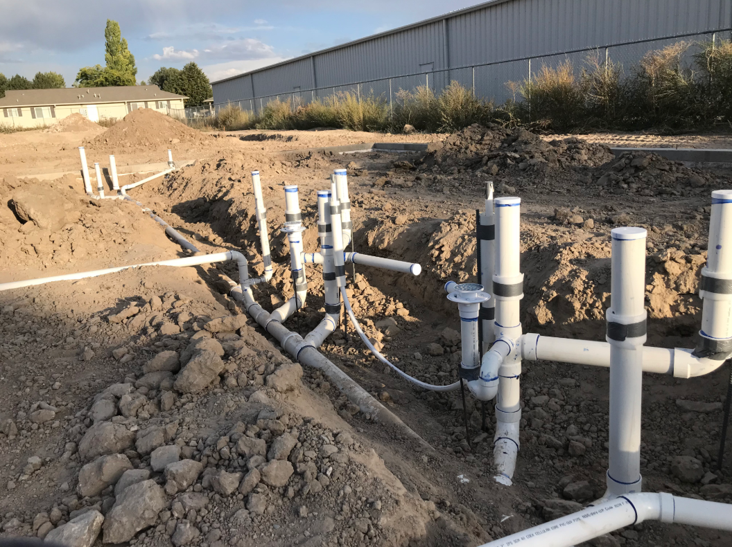 Image: white plumbing pipe laid out in dug out trenches